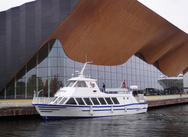 A white boat with blue stripes docked in front of a modern building with a distinctive curved roof. 5