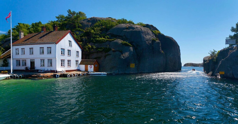 A white house by a rocky coastline with a boat docked nearby. 1