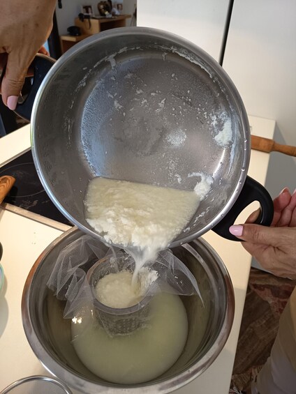 A person pouring a white liquid from a pot into a strainer over a bowl. 3
