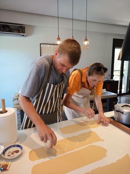 Two people in a kitchen preparing food, with a rolling pin, dough, and kitchen utensils visible. 5