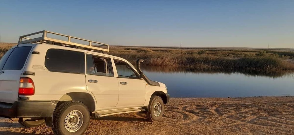 A white SUV parked by a calm body of water with a clear sky. 5