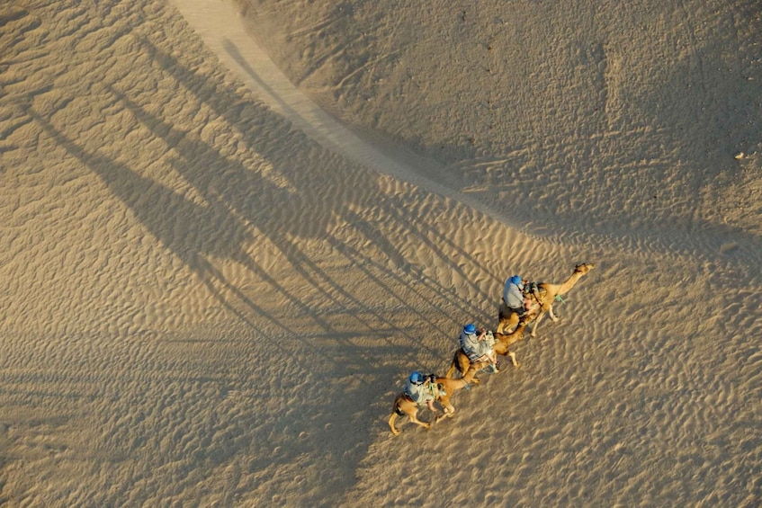 A group of people riding camels in a desert with sand dunes and shadows. 4