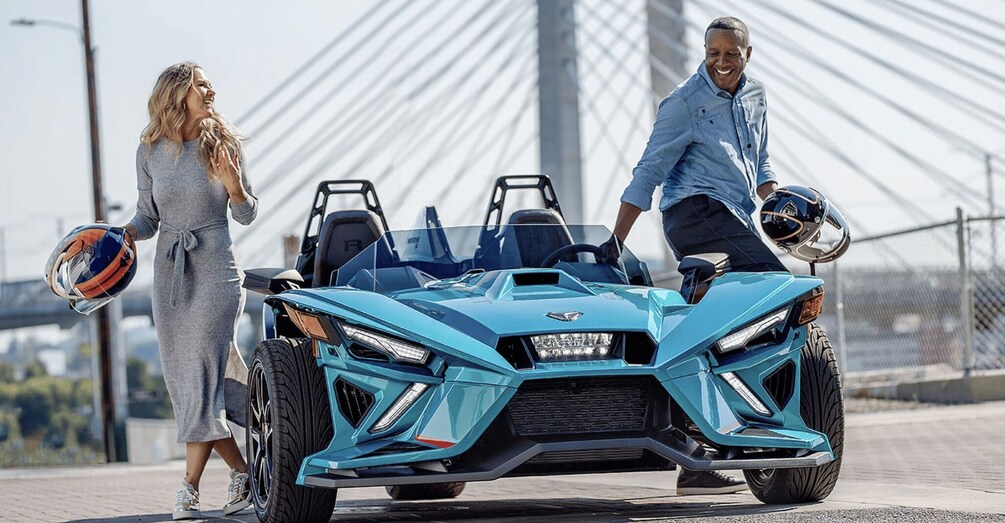 A blue sports car on a bridge with a person holding a helmet. 1