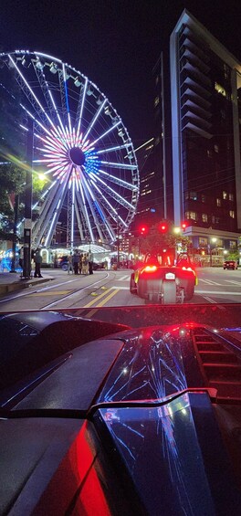 A brightly lit Ferris wheel at night with a car in the foreground. 2
