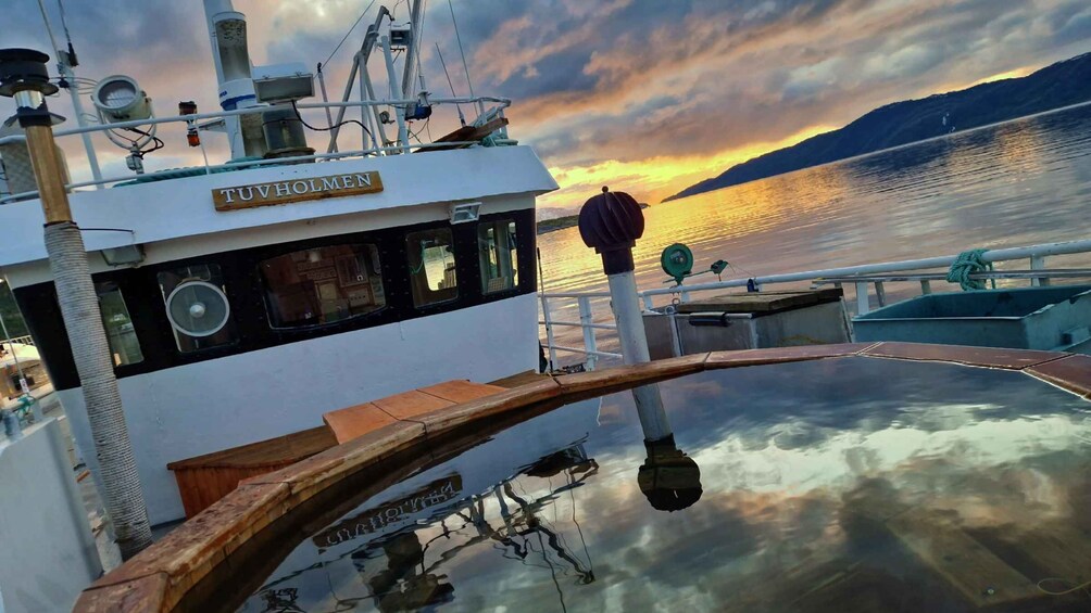 A boat named 'TUVHOLMEN' with a view of a sunset over water and a mountain in the distance. 2
