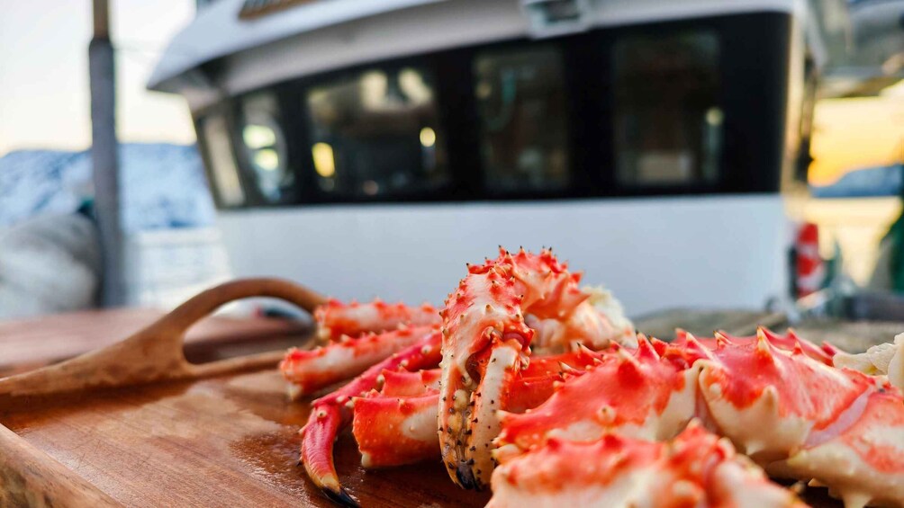A wooden cutting board with crab legs in the foreground and a boat in the background. 1