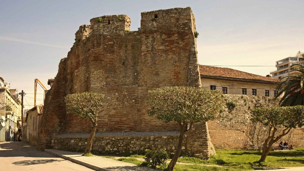 A historic stone castle with a moat, surrounded by modern buildings and a clear sky. 4