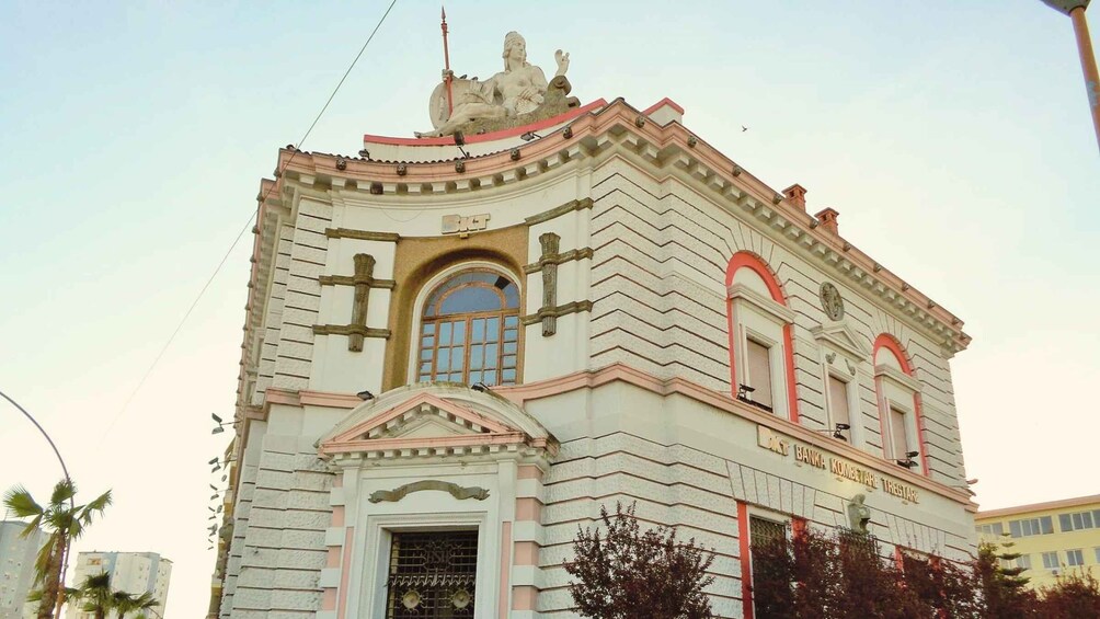 A historic building with classical architecture, featuring a statue on the roof and a prominent entrance. 3