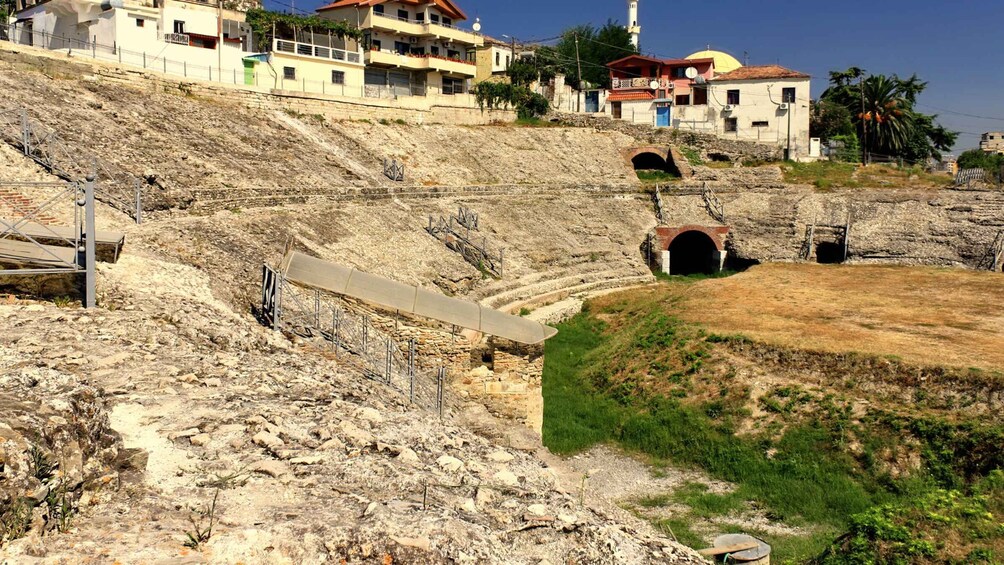 A rocky hillside with a tunnel entrance, a bridge, and residential buildings in the background. 2