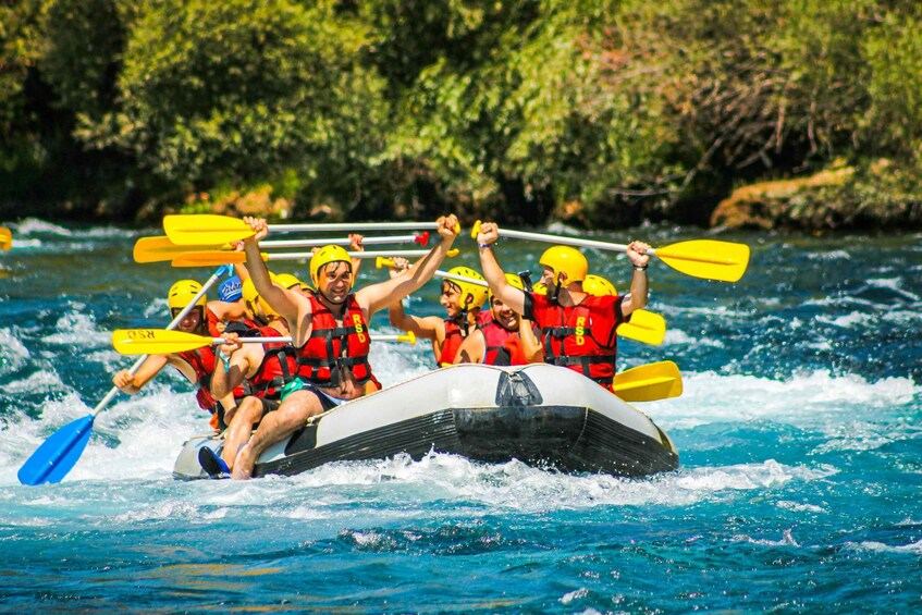 A group of people in a raft on a river, wearing life jackets and paddling with yellow paddles. 4