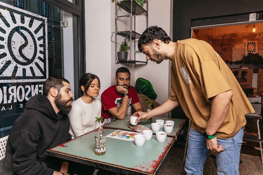 A group of people at a table with cups and a bottle, in a room with a clock and shelves. 2