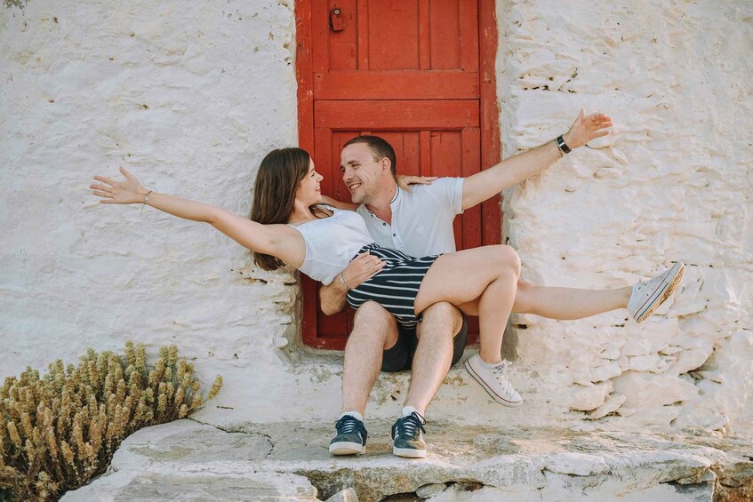 A couple embracing and sitting on a stone ledge with a red door in the background. 4