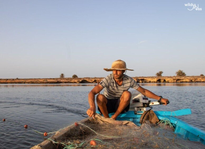 A person fishing by a calm river with sparse vegetation in the background. 2