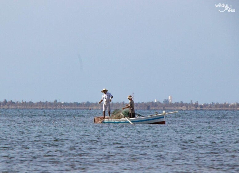 Two people fishing from a small boat on a calm body of water with a distant shoreline. 5
