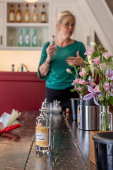 A woman in a green shirt standing behind a bar counter with a bottle of alcohol in front of her. 3