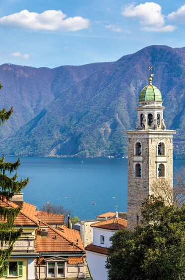 A tower with a green dome and a bell, overlooking a lake with boats, surrounded by mountains. 3