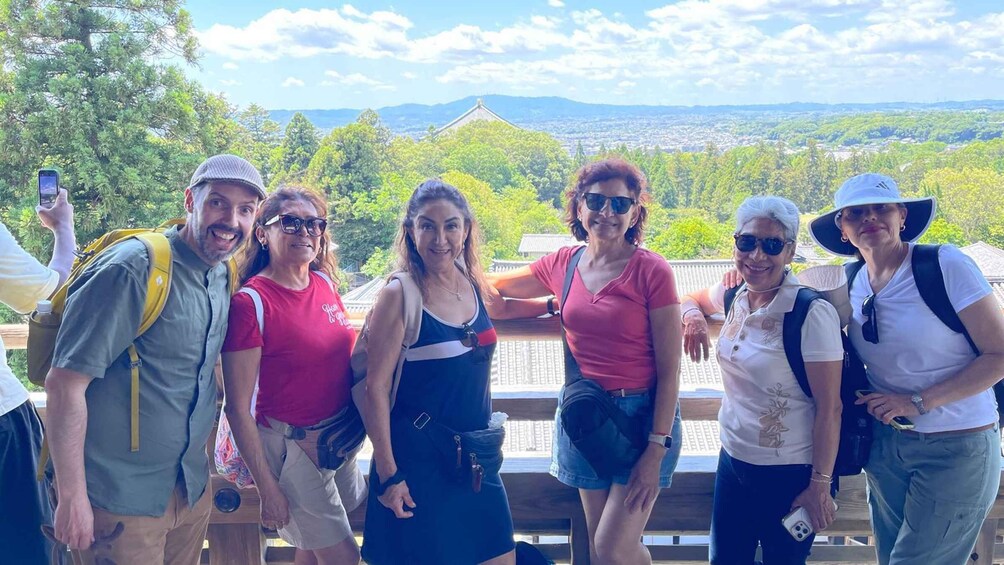 A group of people standing on a wooden platform with a scenic view of a city and mountains in the background. 4