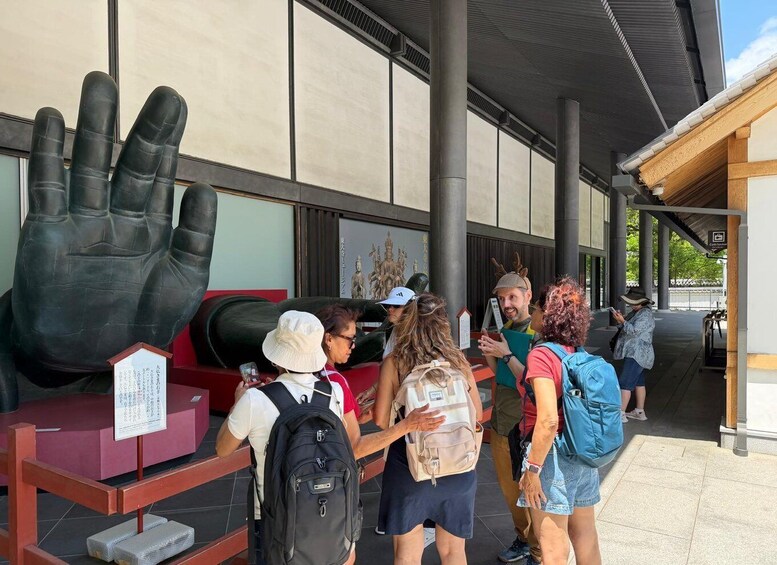 A group of people standing in front of a large hand sculpture and a building with traditional Japanese architecture. 5