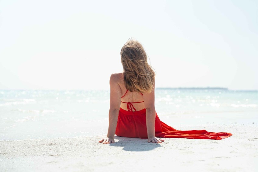 A person sitting on a beach with a red dress, facing the ocean. 3