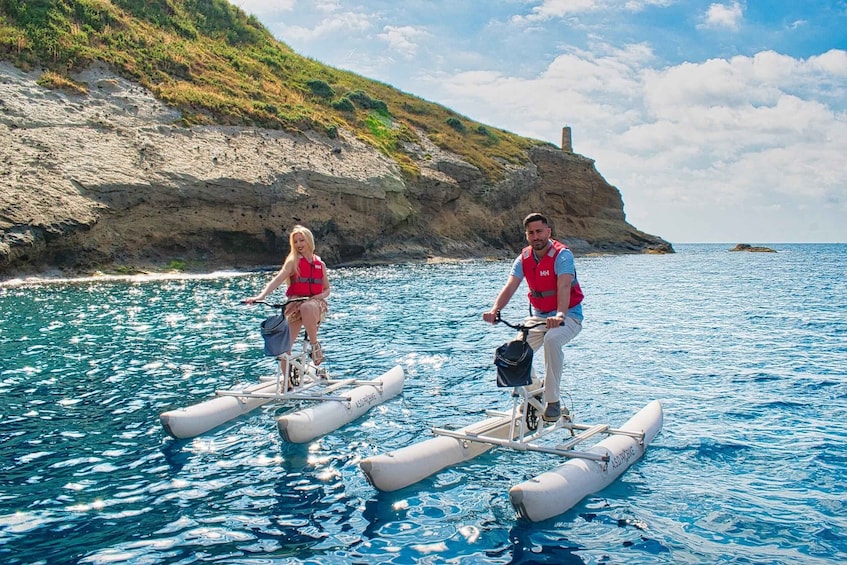 Two people on water bikes in a coastal area with cliffs and a lighthouse. 3