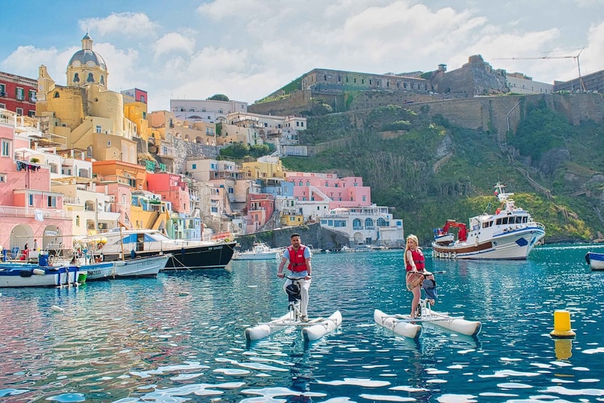 A coastal town with colorful buildings, a historic fort, and people riding inflatable boats. 2