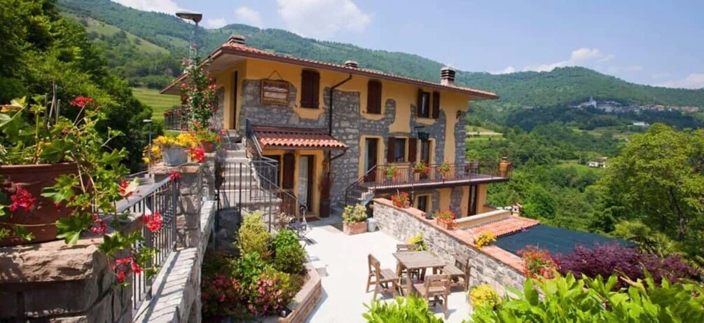 A stone house with a balcony, surrounded by lush greenery and a mountainous backdrop. 3