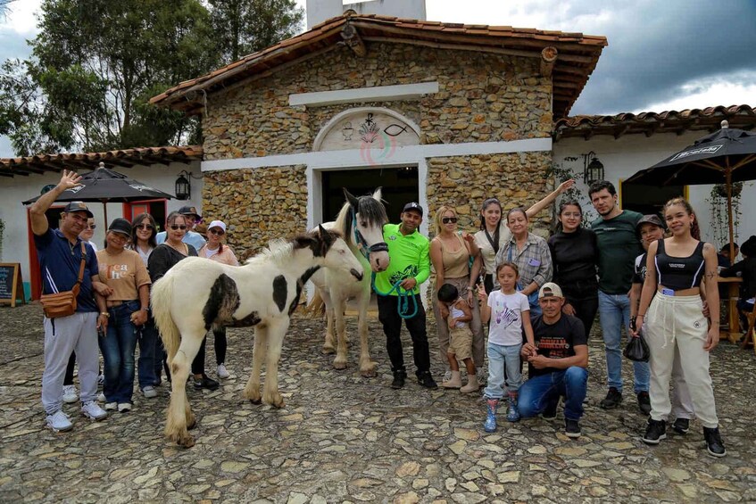 A group of people posing with a horse in front of a stone building with a tiled roof. 1