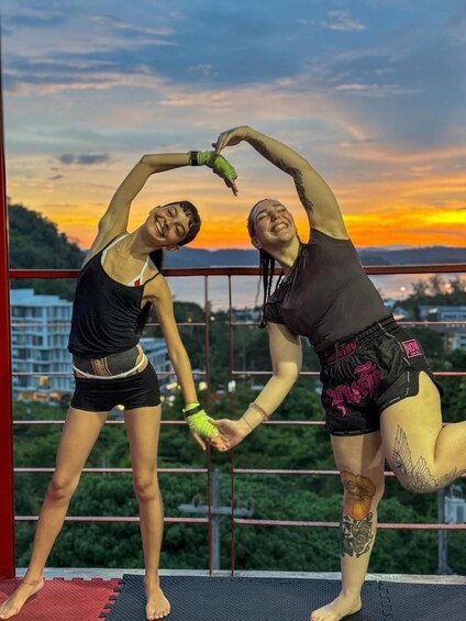 Two people performing a yoga pose on a balcony with a sunset in the background. 3