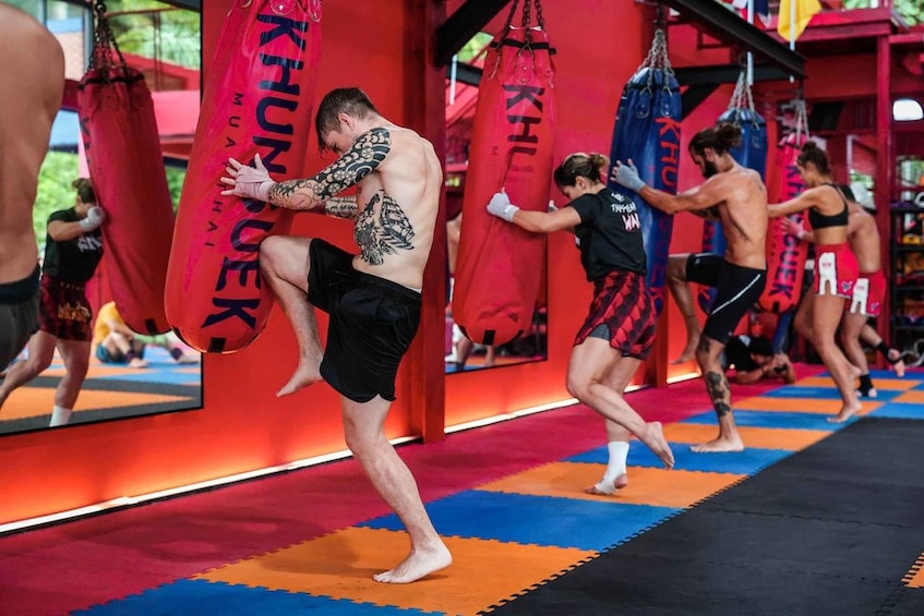 A martial arts training session with participants practicing kicks on red punching bags. 2