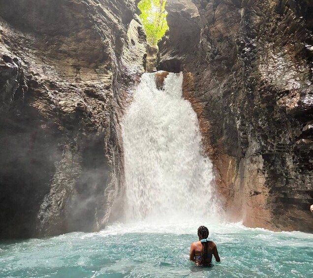 A waterfall in a rocky gorge with a person standing in the water. 1