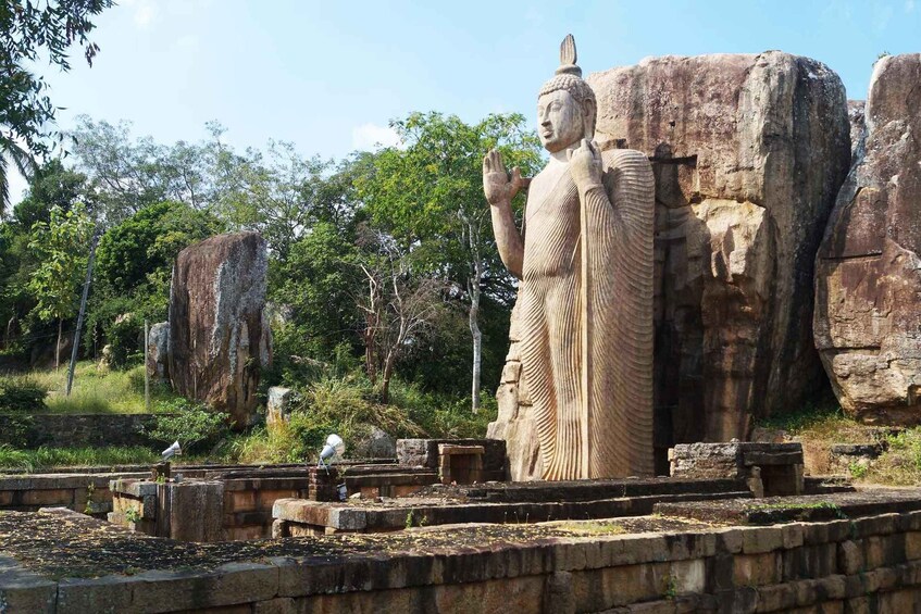 A large stone statue of a figure in a traditional pose, set against a backdrop of natural rock formations and trees. 5