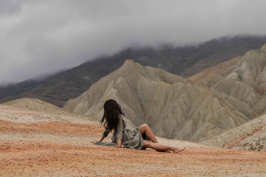 A person sitting on a sandy terrain with a mountainous backdrop. 3