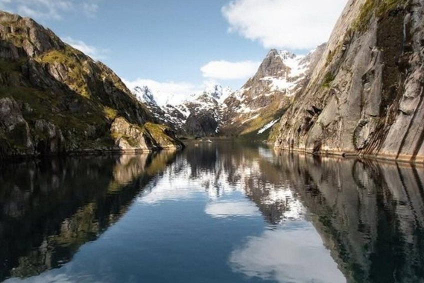 A calm lake surrounded by mountains with snow-capped peaks and rocky cliffs. 2