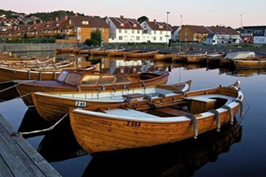 A marina with wooden boats docked, calm water, and houses in the background. 2