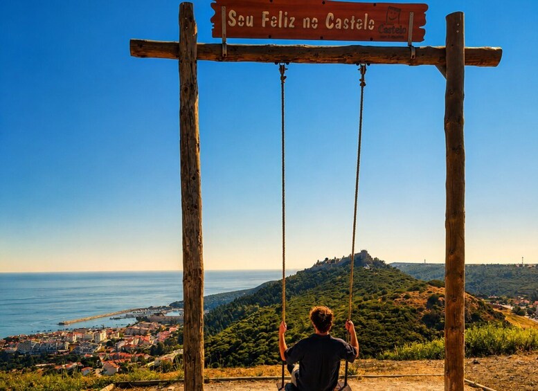 A person sitting on a swing overlooking a coastal town and a hilltop castle. 4