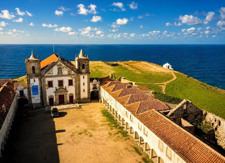 A coastal fort with a church, a long wall, and the ocean in the background. 1