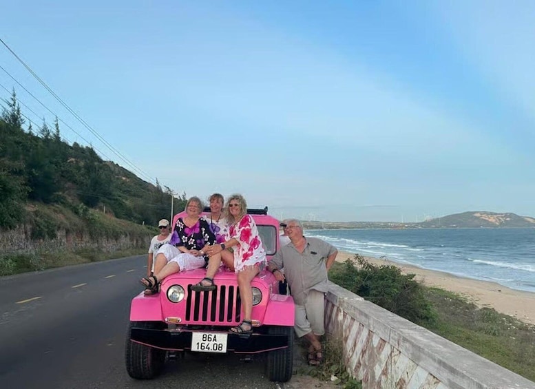 A pink vehicle with four passengers on a coastal road. 4