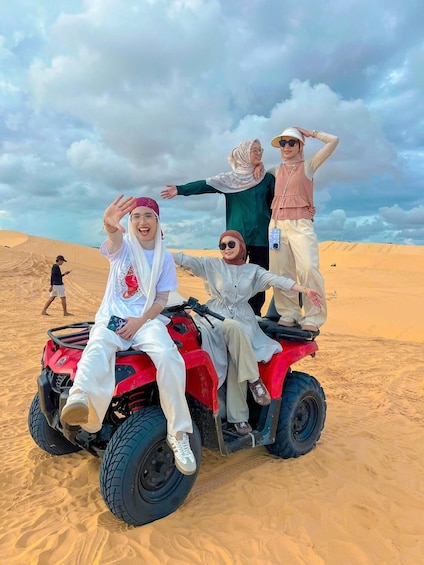 A group of people on a red quad bike in a desert with sand dunes. 2