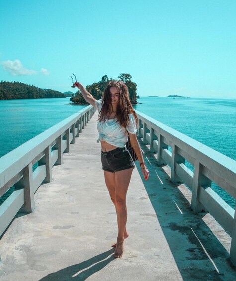 A person walking on a concrete pier with a turquoise sea and green hills in the background. 3