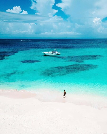 A beach with clear turquoise water, a boat, and a person standing on the shore. 1