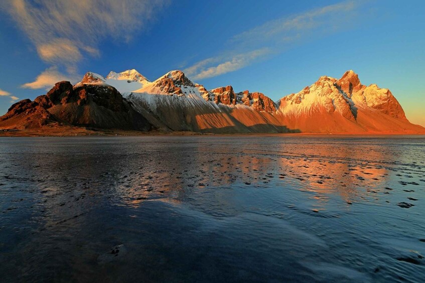 A mountain range with snow-capped peaks and a calm body of water reflecting the mountains. 5
