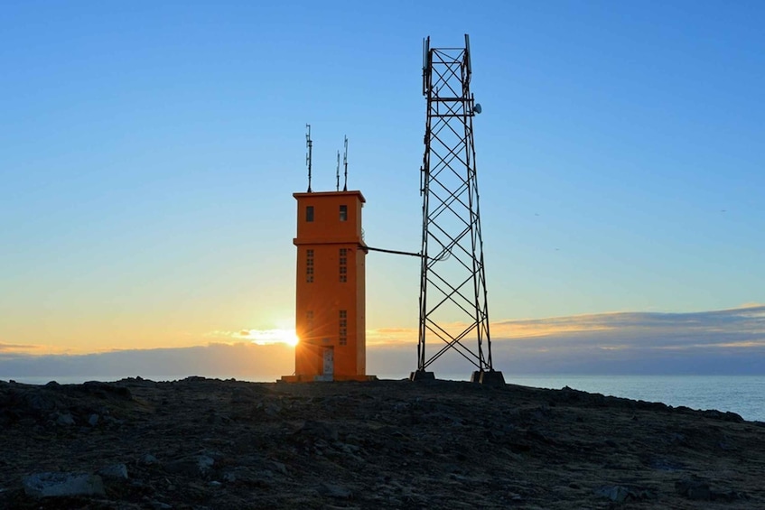 A coastal landscape with a tall communication tower and a small orange building during sunset. 4