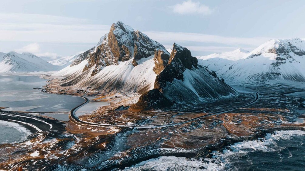A mountainous landscape with snow-covered peaks, a winding road, and a body of water. 2
