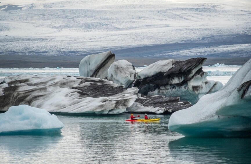 Kayakers on a calm body of water with large ice formations in the background. 5