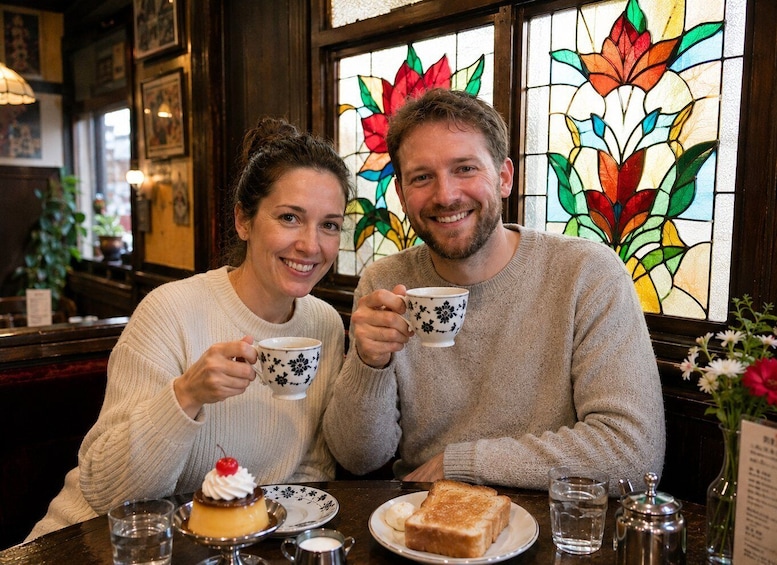 Two people sitting at a table with a cake and toast, holding coffee cups, in a cafe with stained glass windows. 1