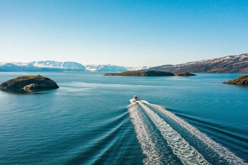 A boat creating a wake on a calm lake surrounded by mountains. 1