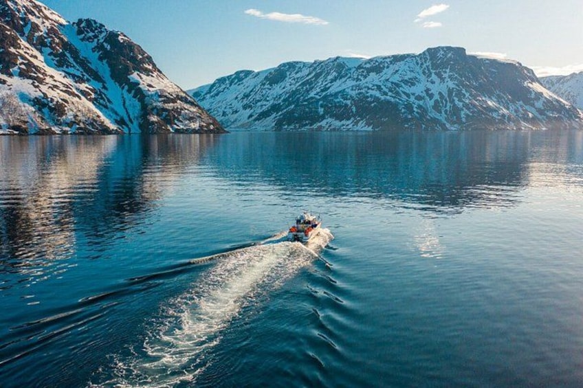 A boat speeding across a calm lake surrounded by snow-covered mountains. 5
