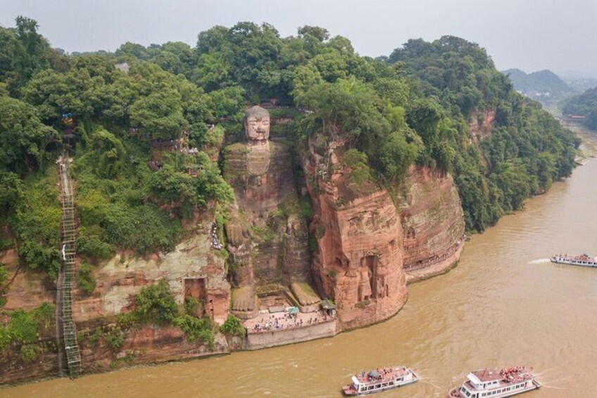 A large Buddha statue on a cliff by a river with boats and a ladder. 3