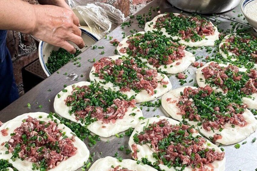 A person preparing dumplings with meat and chopped green onions on a stainless steel surface. 5