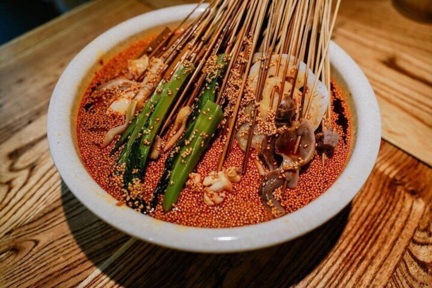 A bowl of spicy dish with green vegetables and skewers. 4